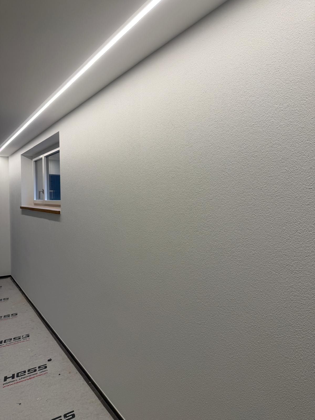 Wand mit feinem Strukturputz im Streiflicht einer LED-Leiste an der Decke, am Boden Abdeckpapier